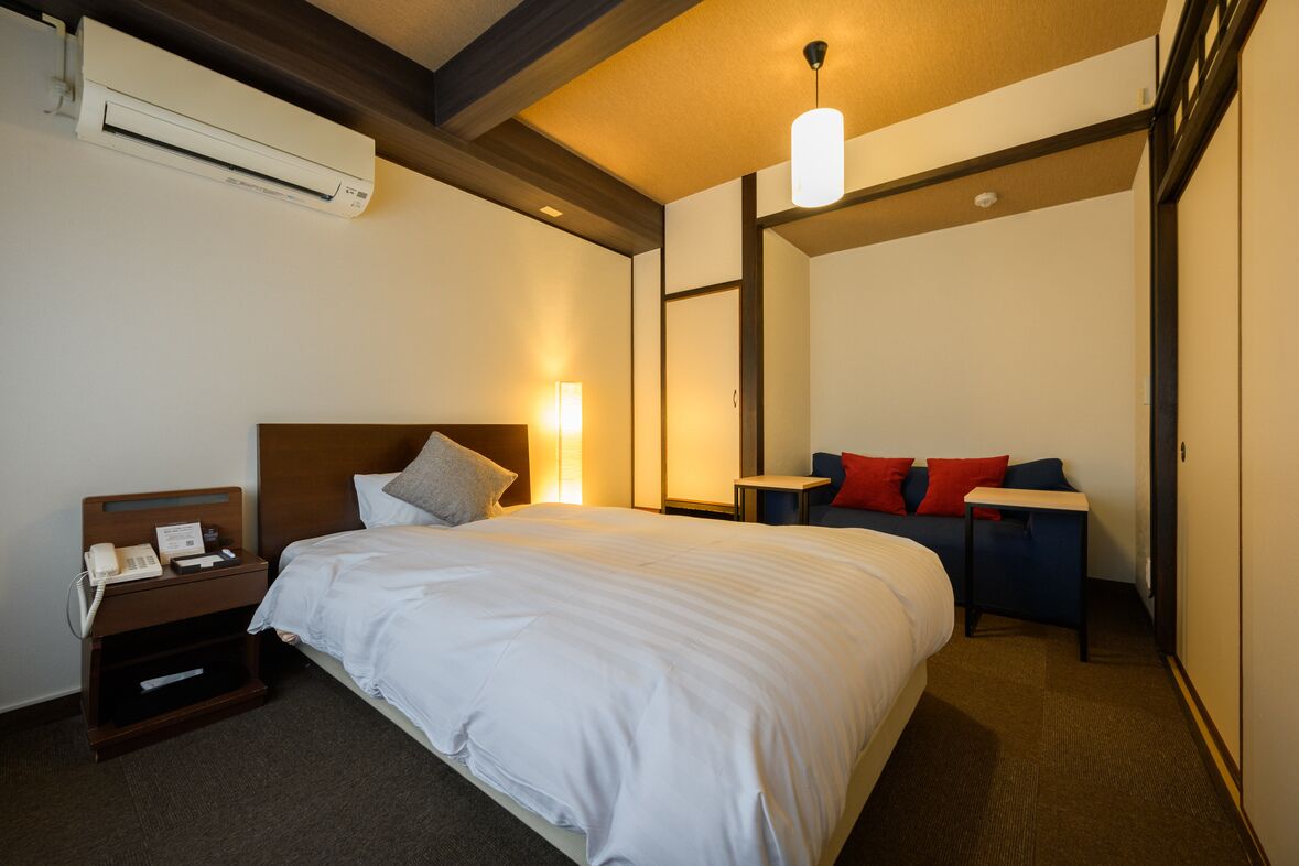A hotel room with a bed, bedside table, lamp, and an air conditioning unit.