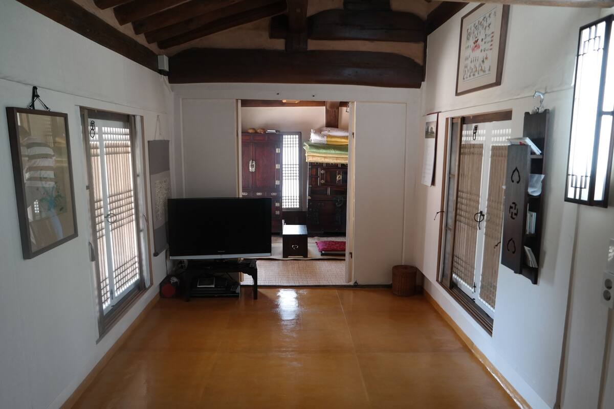 A hallway with a wooden floor, a television on a stand, and a door leading to another room.