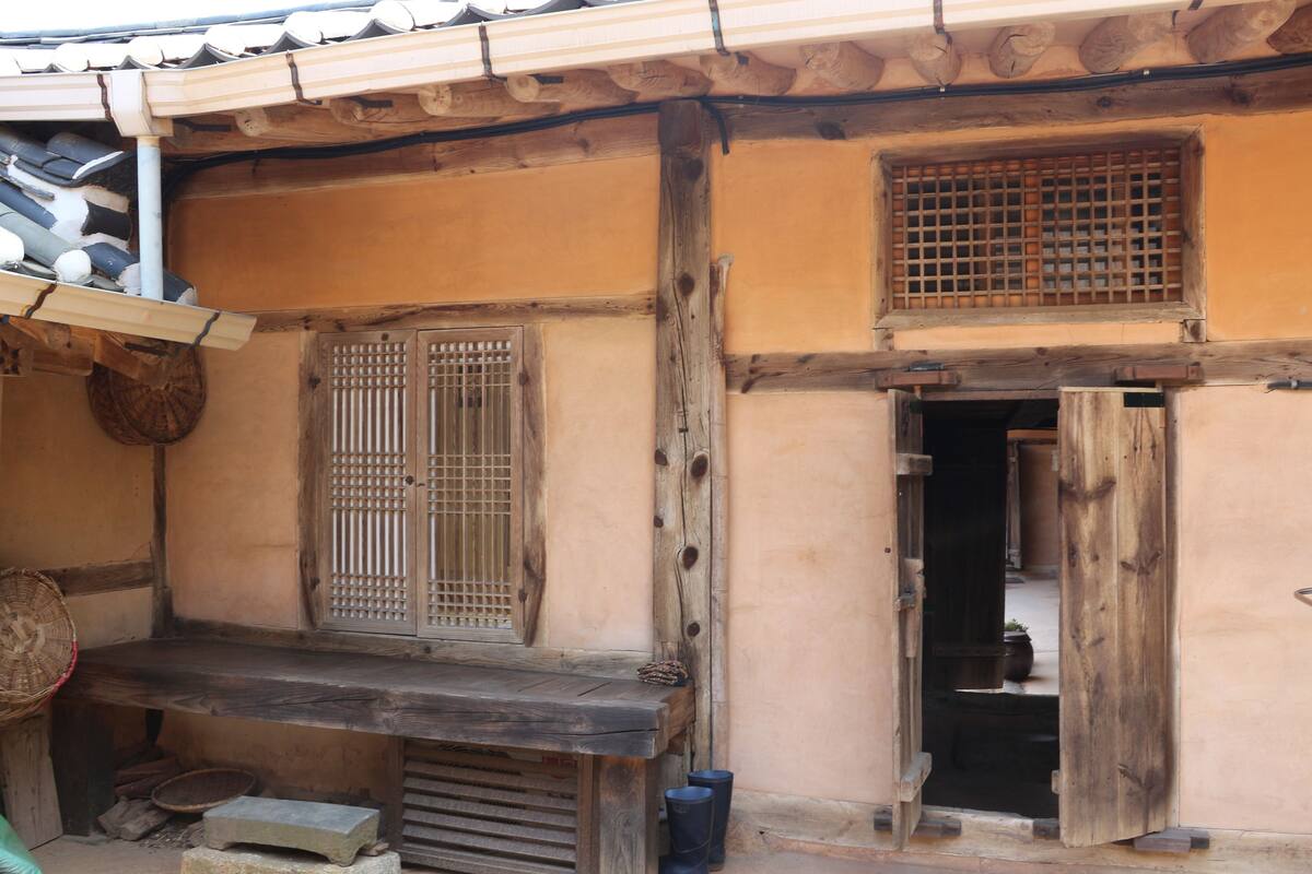 A traditional wooden building with a wooden bench, a window with a grid pattern, and a door leading inside.