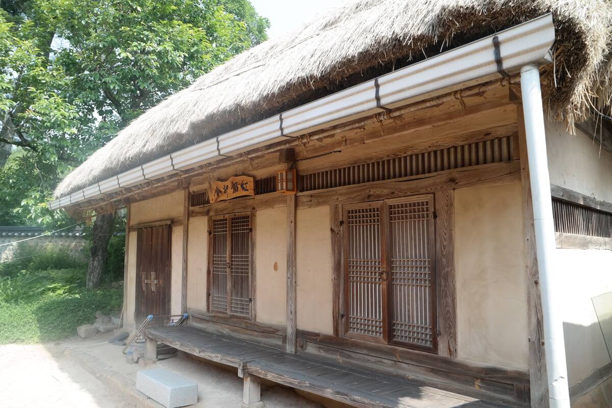 A traditional wooden building with a thatched roof, wooden lattice windows, and a small porch.