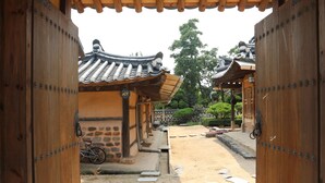 A traditional wooden gate leading to a courtyard with a tiled roof structure, a bicycle, and stone steps. - Gyeamgotaek (Seosan)