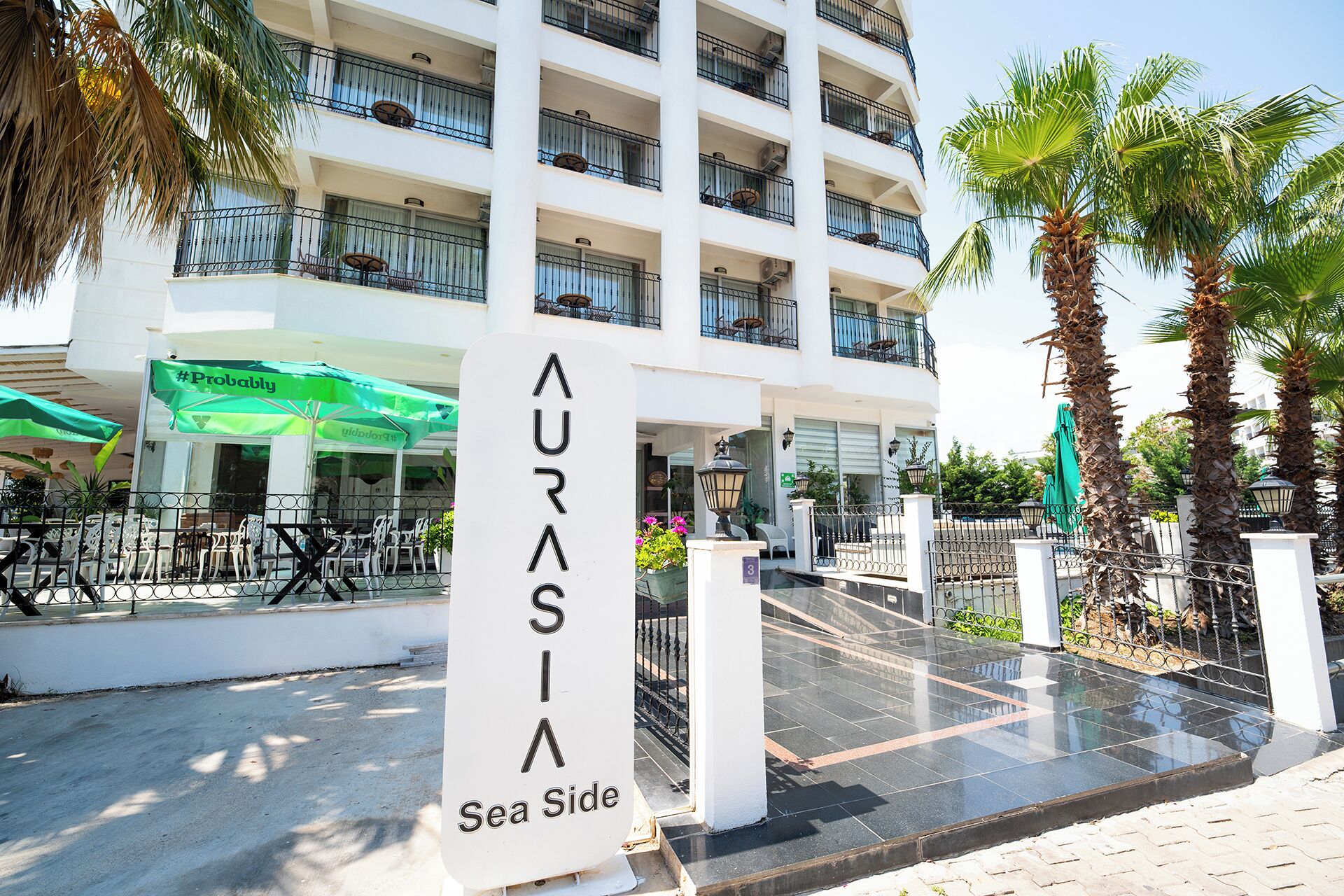 A multi-story hotel with balconies, outdoor seating, and palm trees.