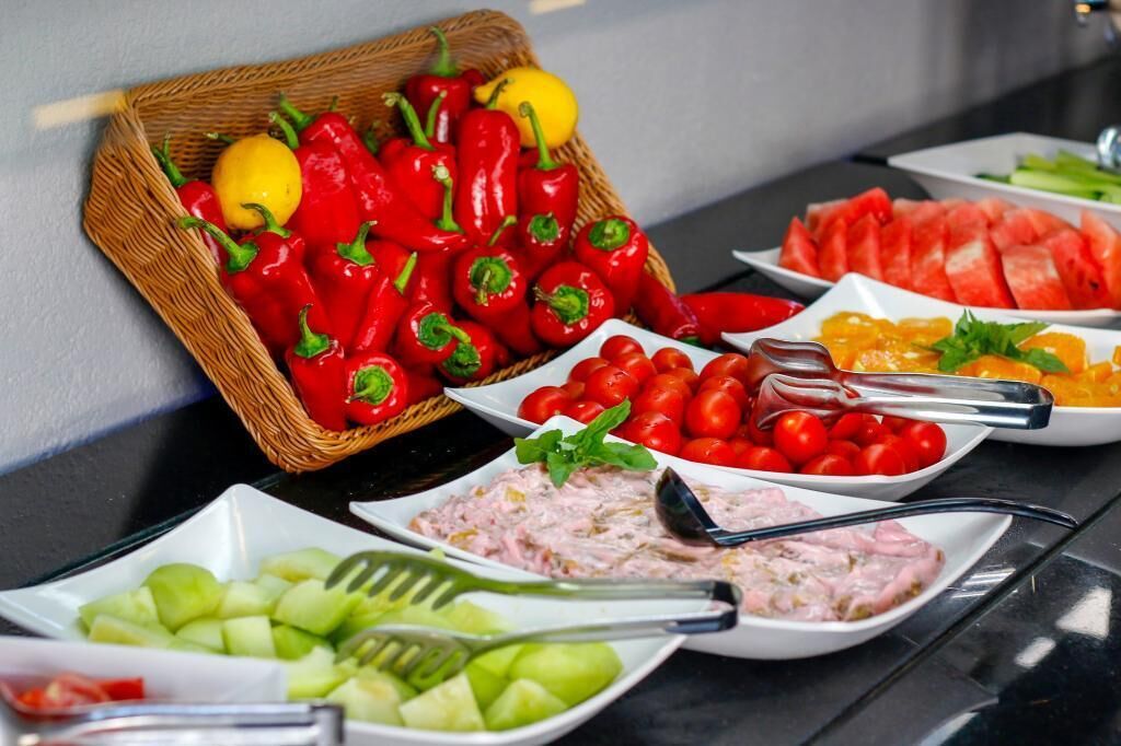A buffet with various dishes including red bell peppers, watermelon, cherry tomatoes, and a salad.