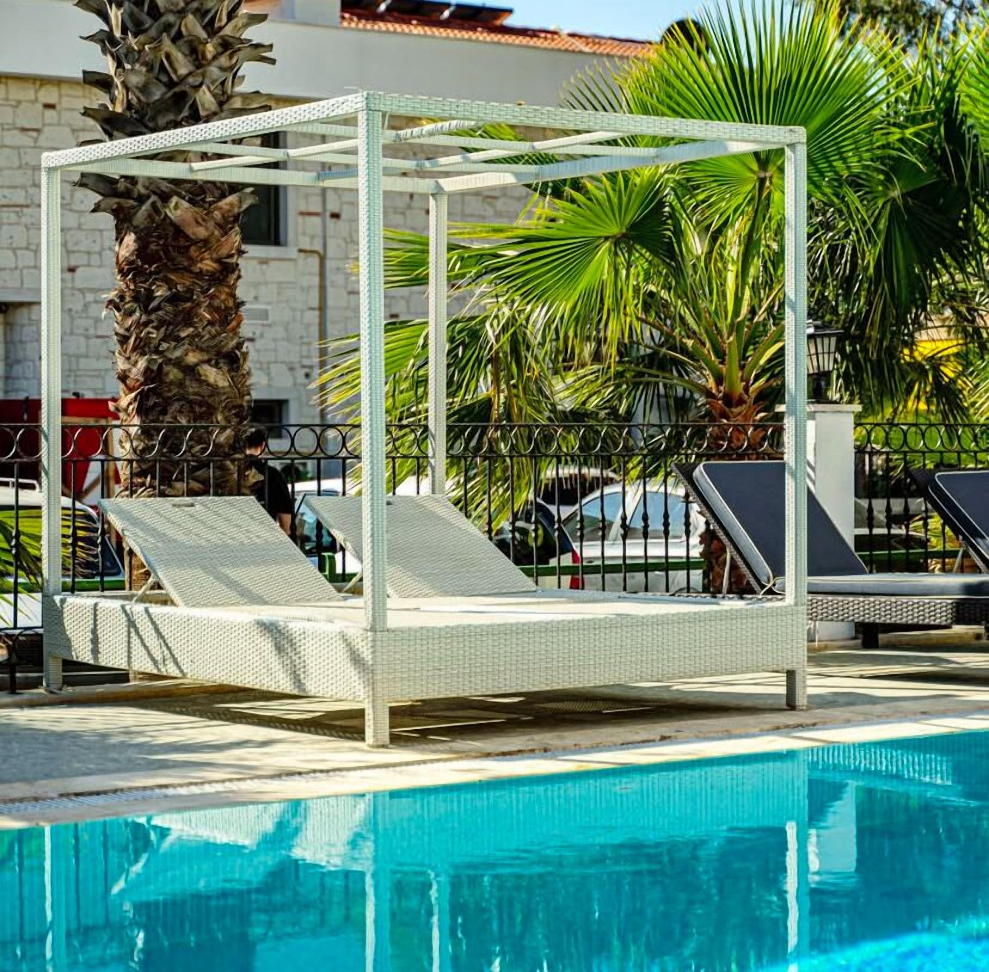 A poolside area with a white canopy bed, palm trees, and a clear blue pool.