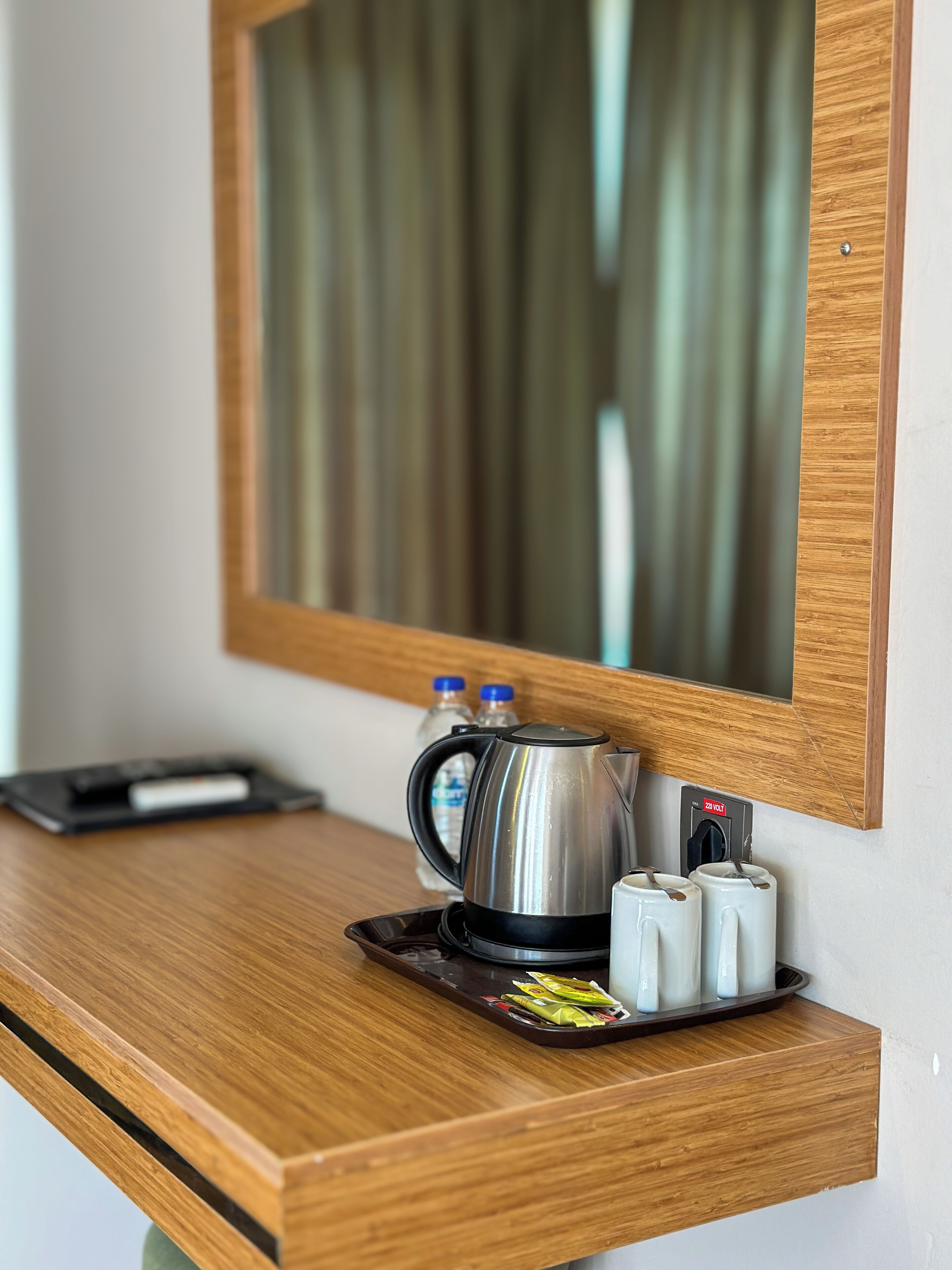 A wooden counter with a stainless steel kettle, a tray with condiments, and a mirror above.