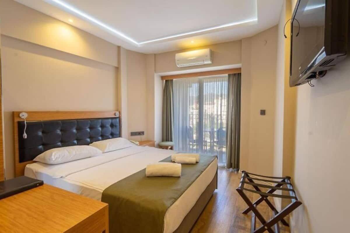 A hotel room with a bed, bedside table, and a TV mounted on the wall.