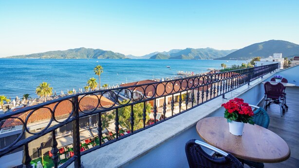 A balcony with a view of the sea, a table with a flower vase, and outdoor seating. - Aurasia SeaSide Hotel (Marmaris)