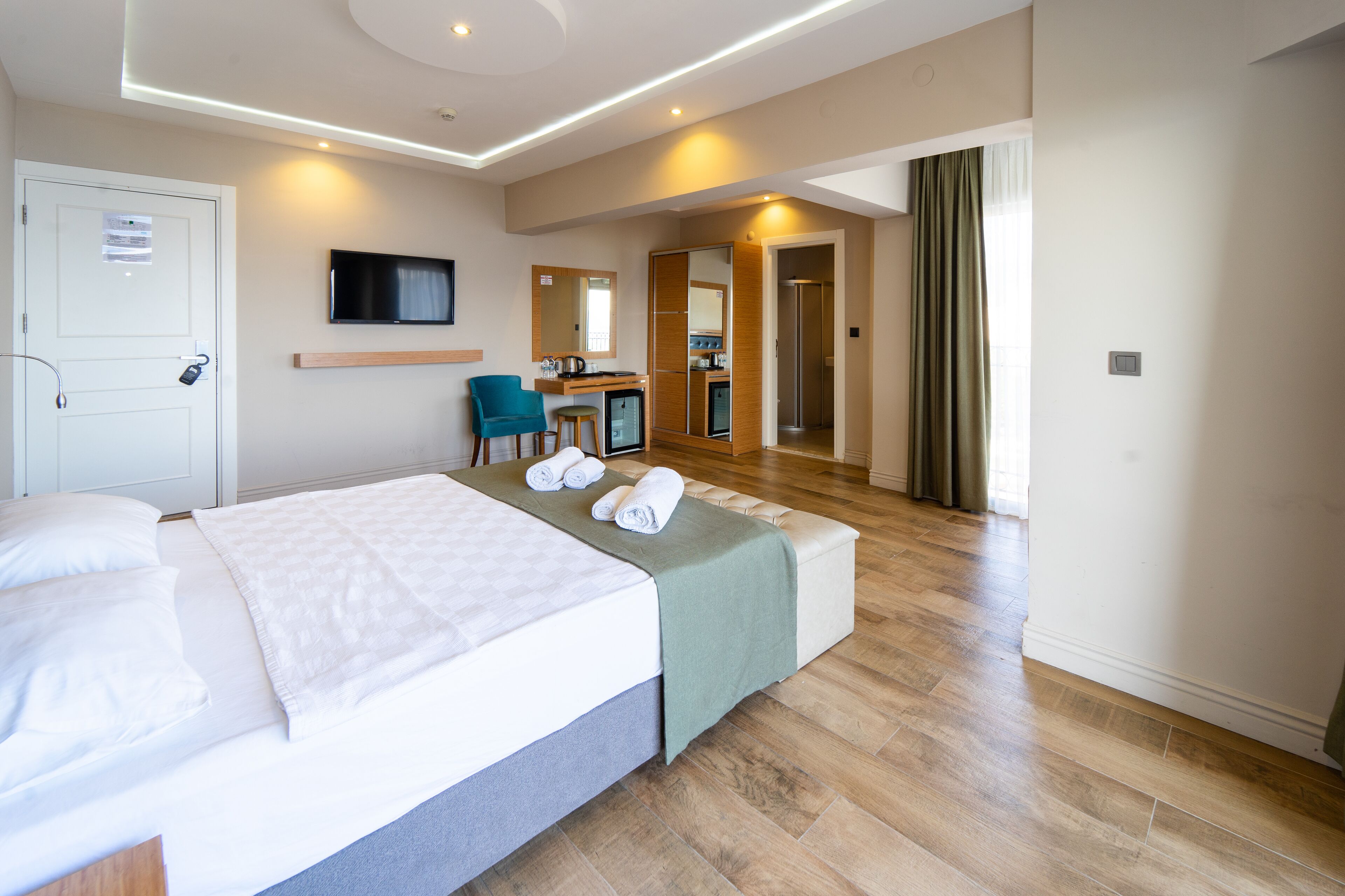 Quarto de hotel com cama, escrivaninha, cadeira, televisão e espelho.