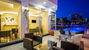 An outdoor seating area with wicker furniture and a glass table, overlooking a pool. - Aurasia SeaSide Hotel (Marmaris)