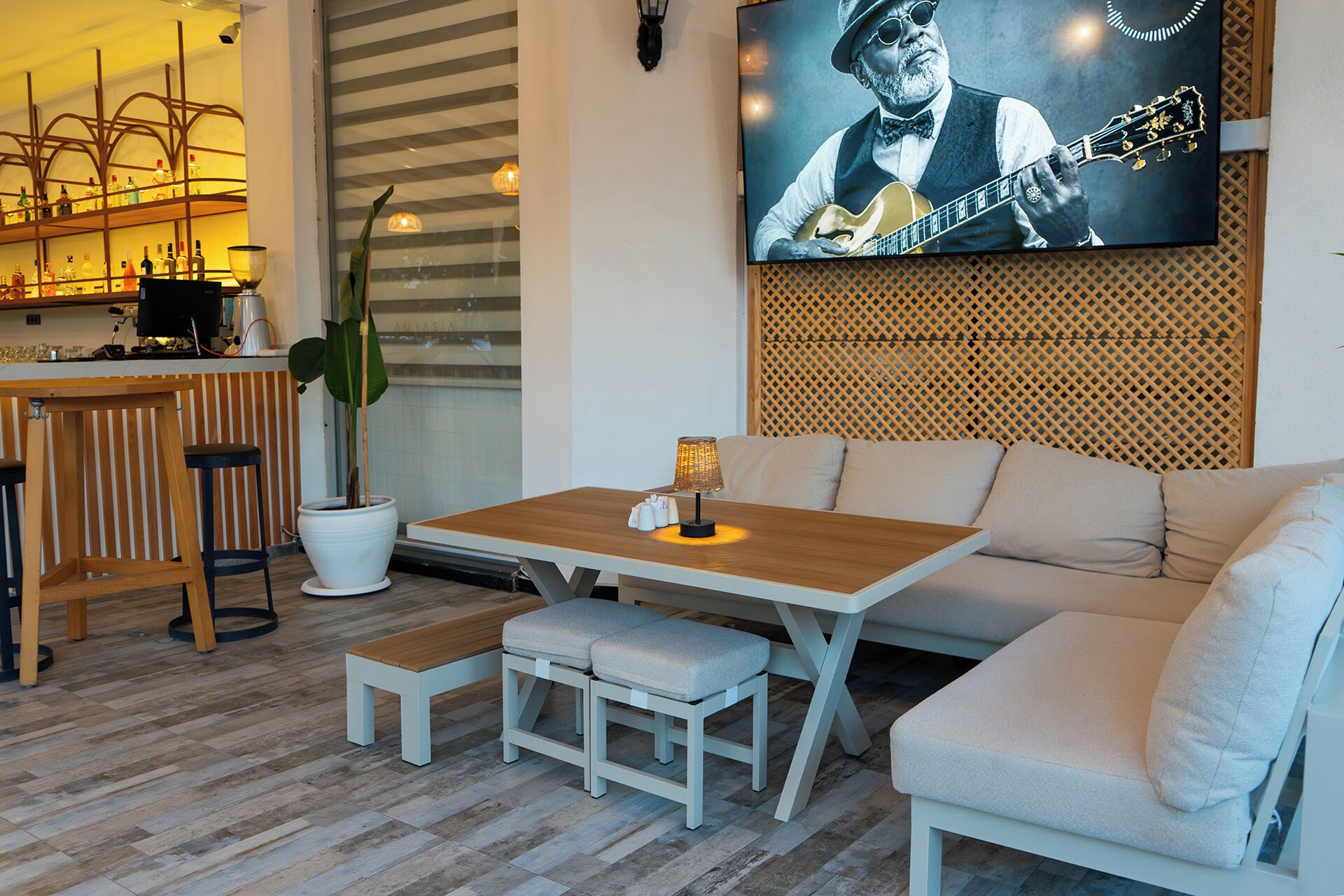 Un salón moderno con una mesa de madera, un banco y un sofá, un televisor en la pared y una barra con botellas.