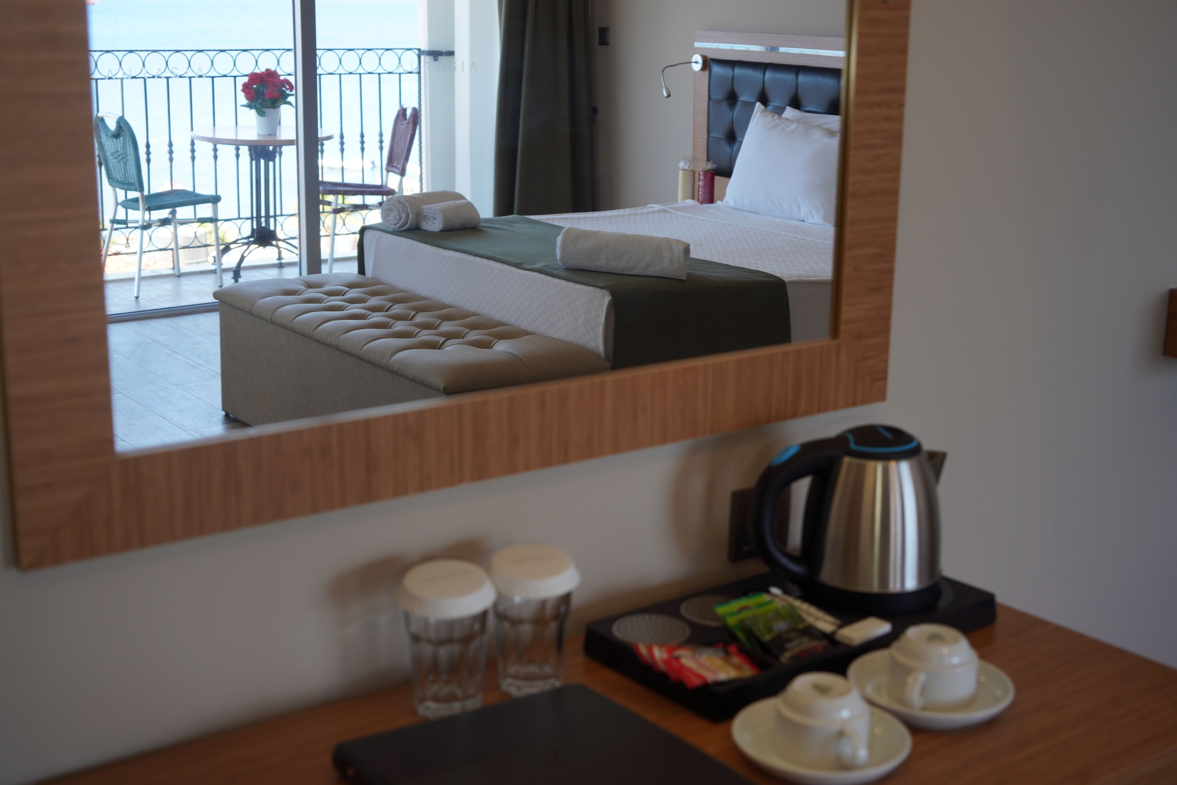 A hotel room with a bed, a sitting area with a bench, a coffee station, and a view of the balcony.