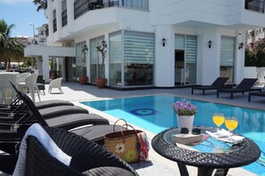 A poolside area with lounge chairs, a table with drinks, and a building with large windows and balconies. - Aurasia SeaSide Hotel (Marmaris)
