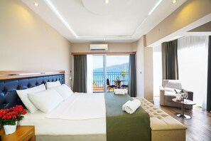 A hotel room with a large bed, a green sofa, a balcony with a table and chairs, and a view of the sea. - Aurasia SeaSide Hotel (Marmaris)