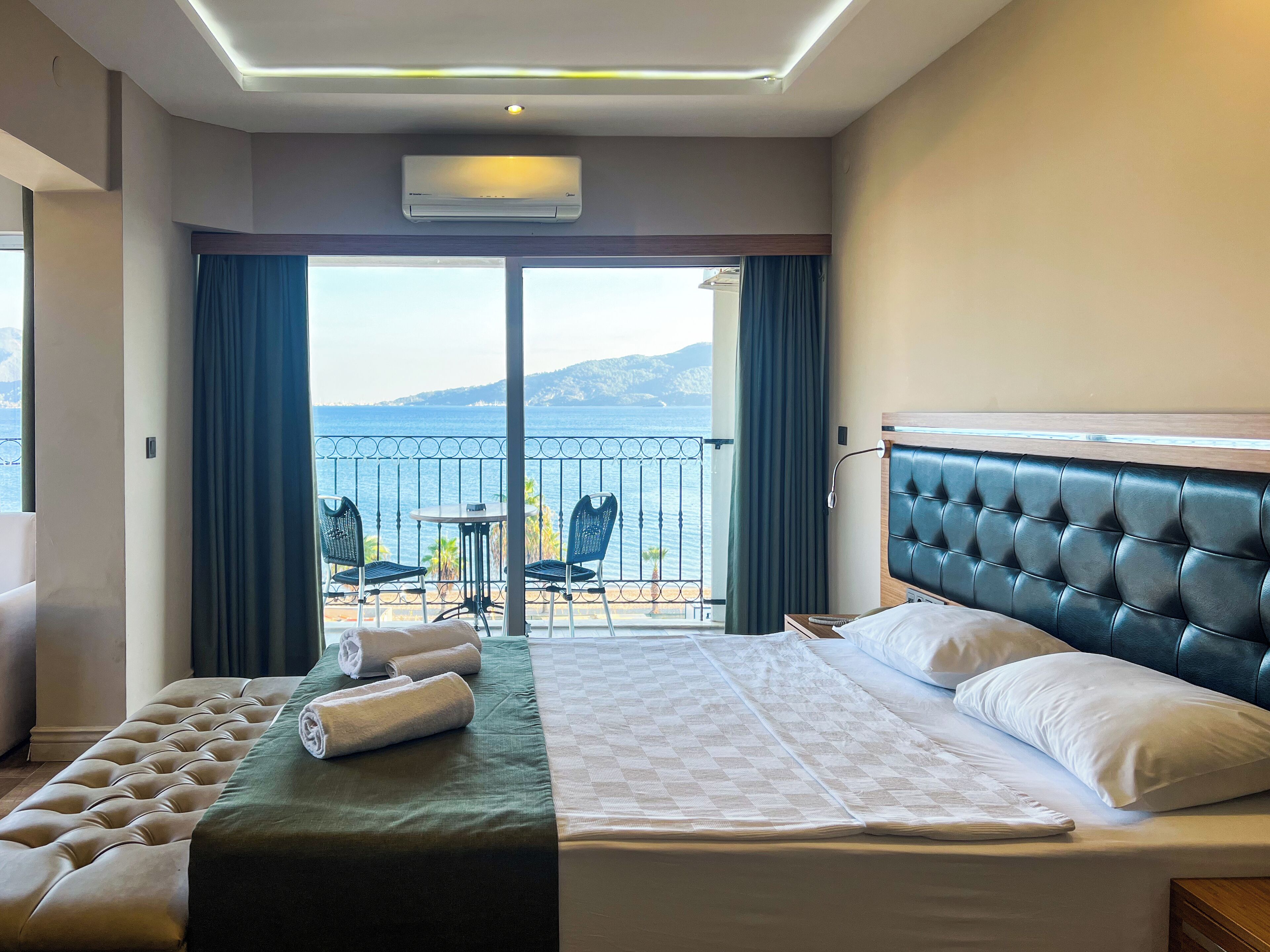 A hotel room with a bed, a balcony with a table and chairs, and a view of the sea.