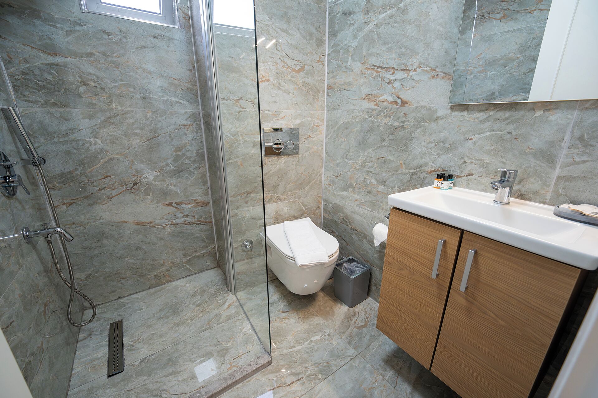 Een badkamer met een douche, toilet, wastafel en houten kasten.
