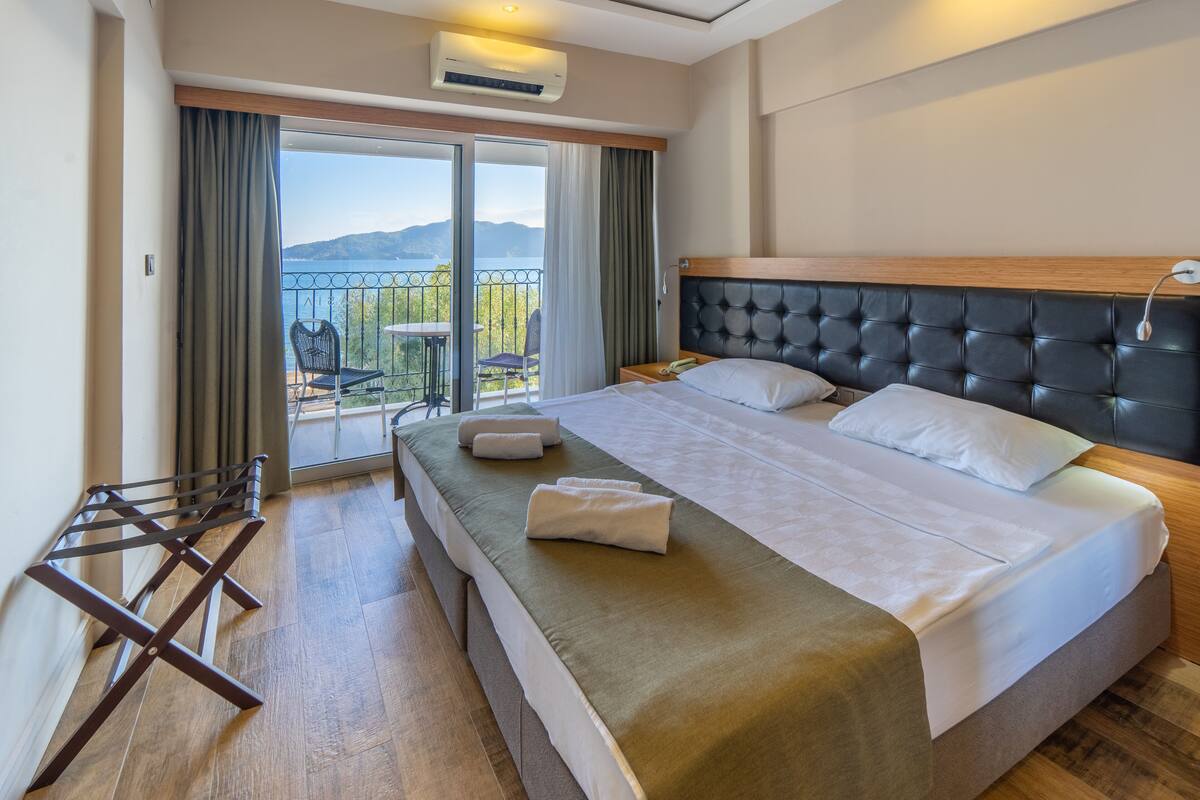 A hotel room with a bed, a balcony with a view, and a wooden floor.