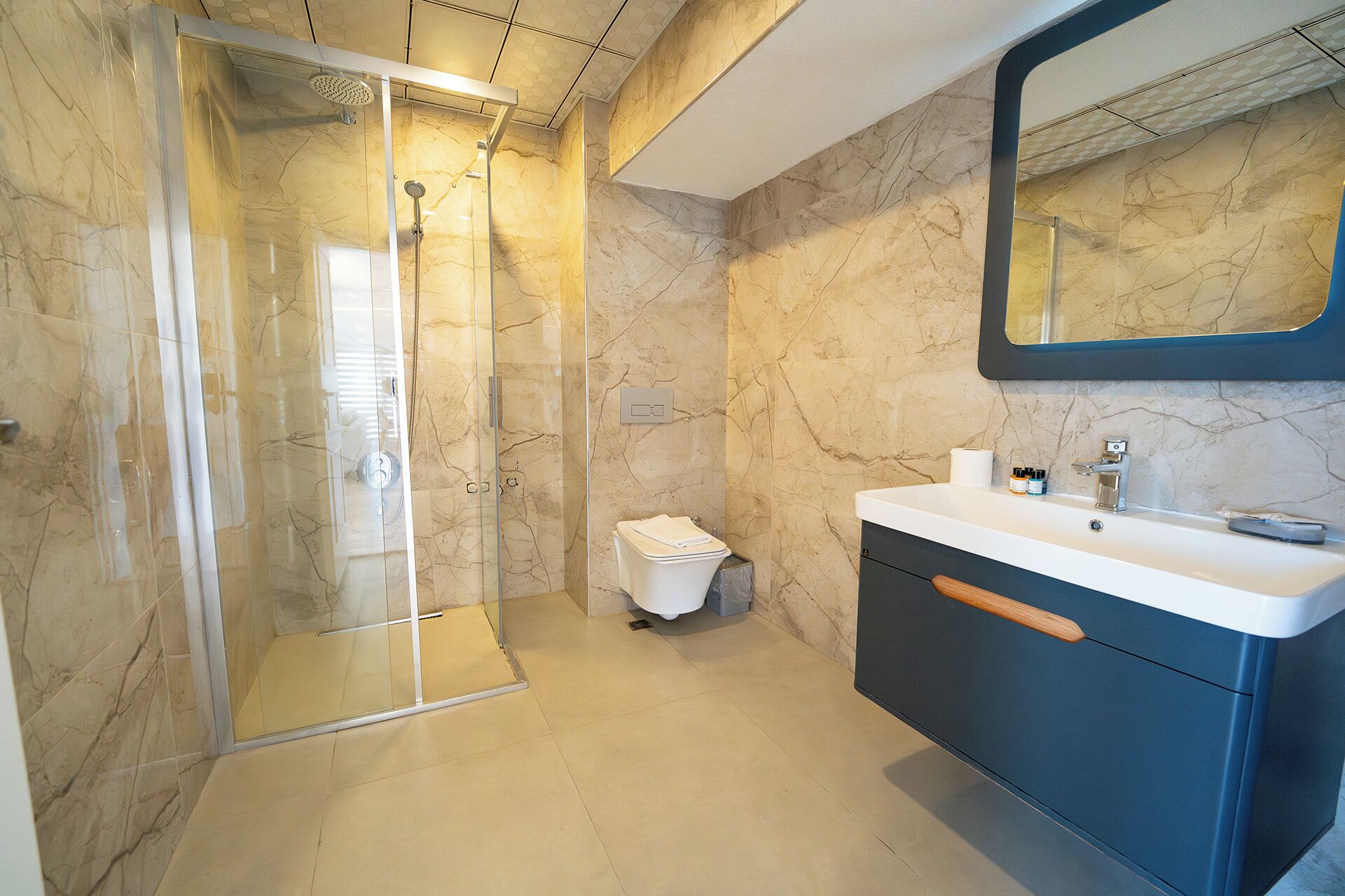 Ein modernes Badezimmer mit einer gläsernen Duschkabine, einem weißen Waschbecken und einer Wand mit Marmorfliesen.