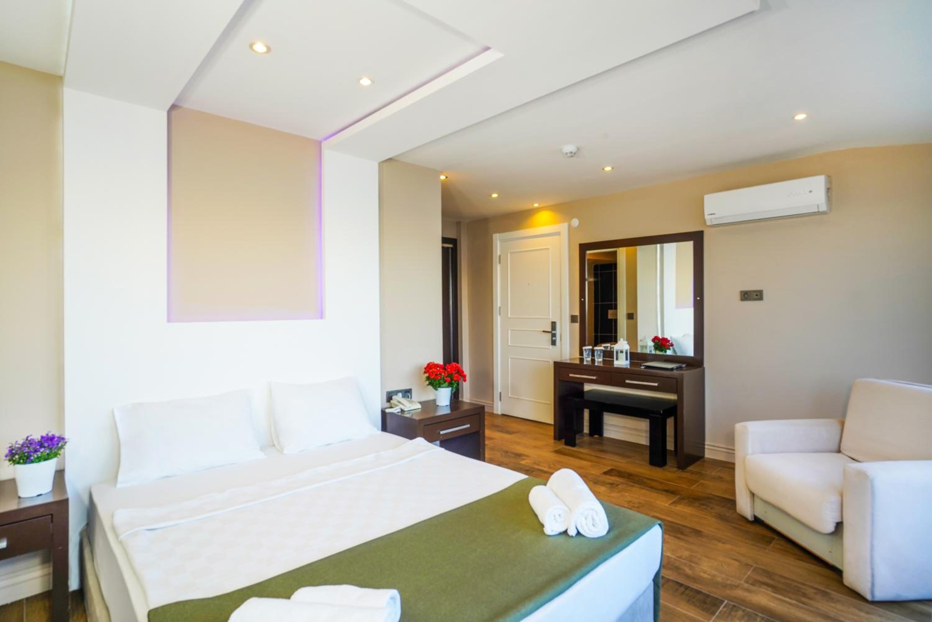 A hotel room with a bed, bedside table, chair, and a desk with a mirror.