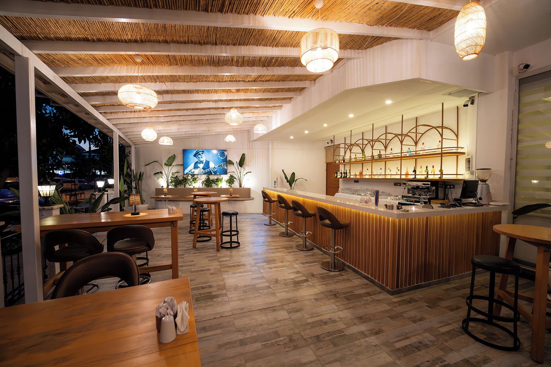 Un restaurante con zona de bar, mesas de madera y luces colgantes.