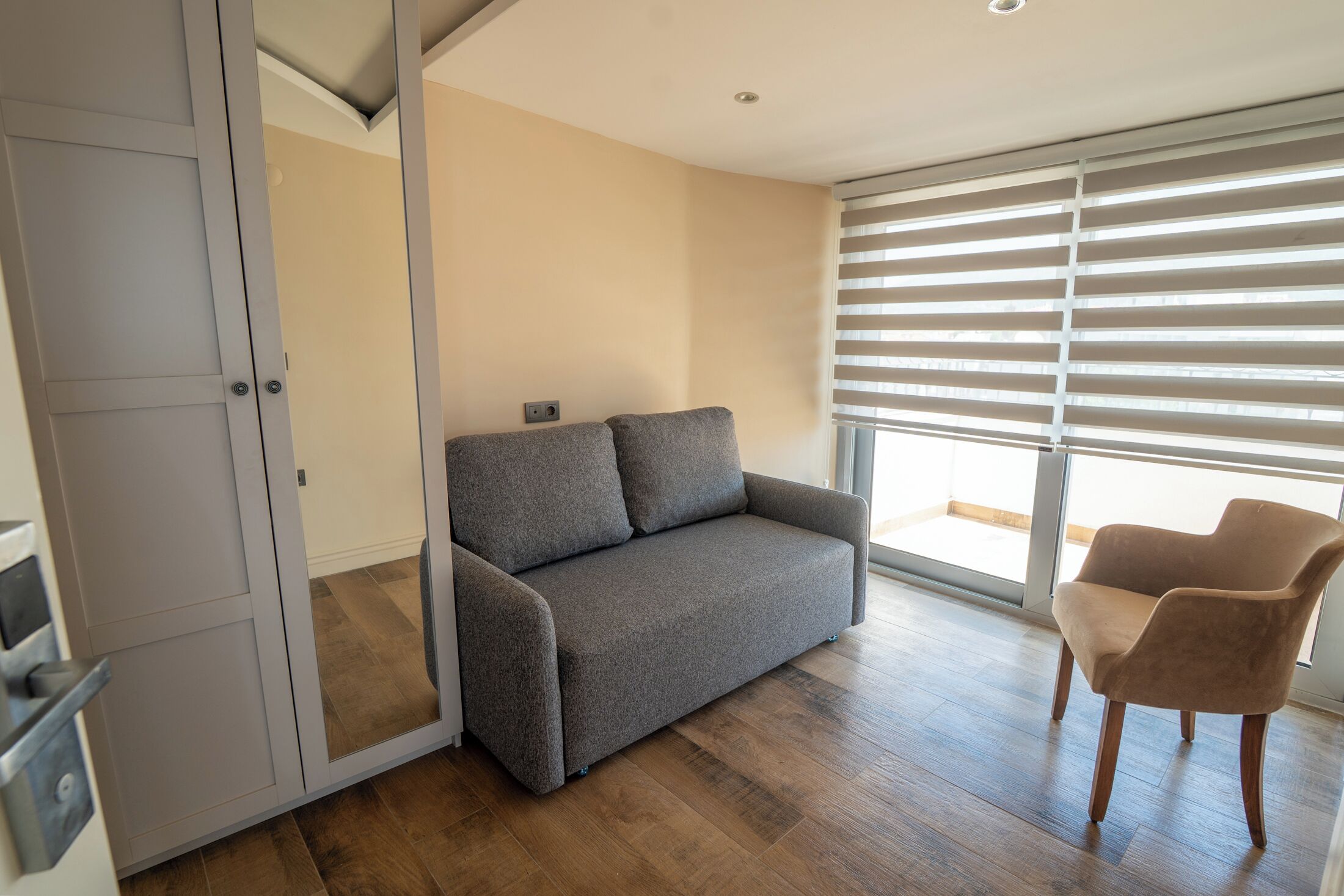 A modern living room with a grey sofa, a brown armchair, and a sliding glass door to the outside.