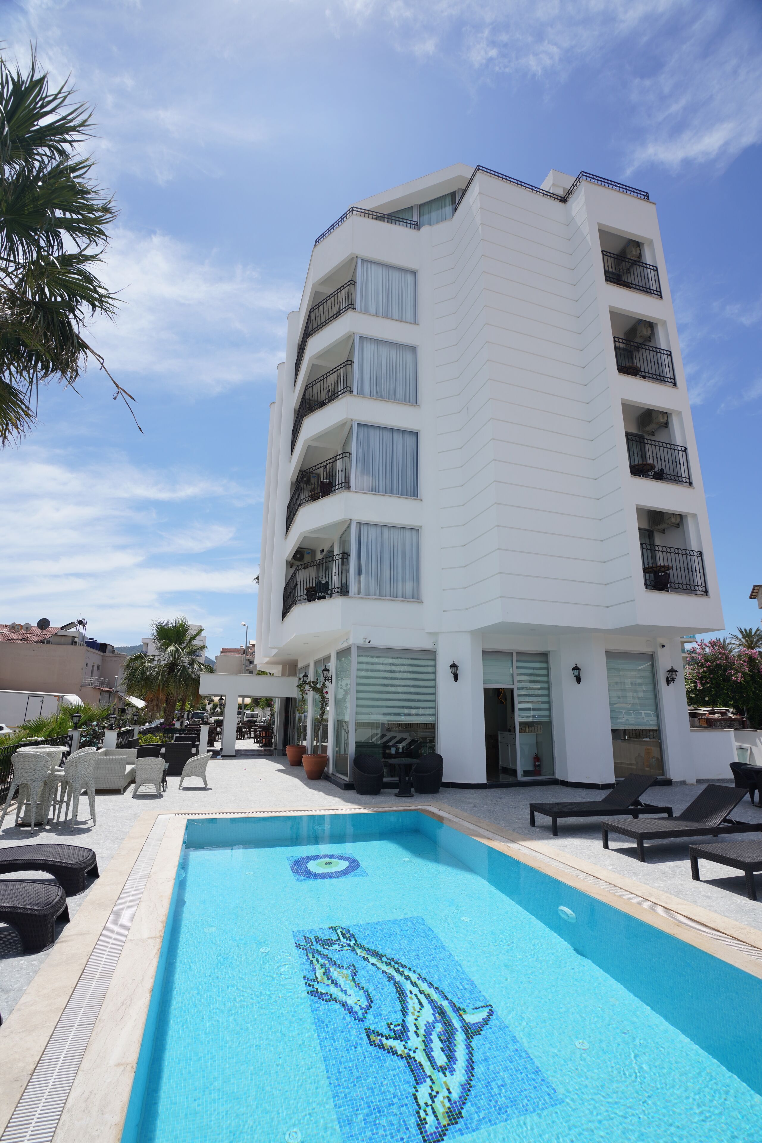 A modern building with a swimming pool, lounge chairs, and a palm tree.