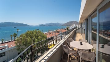 A balcony with outdoor seating overlooking a coastal area with boats and mountains.