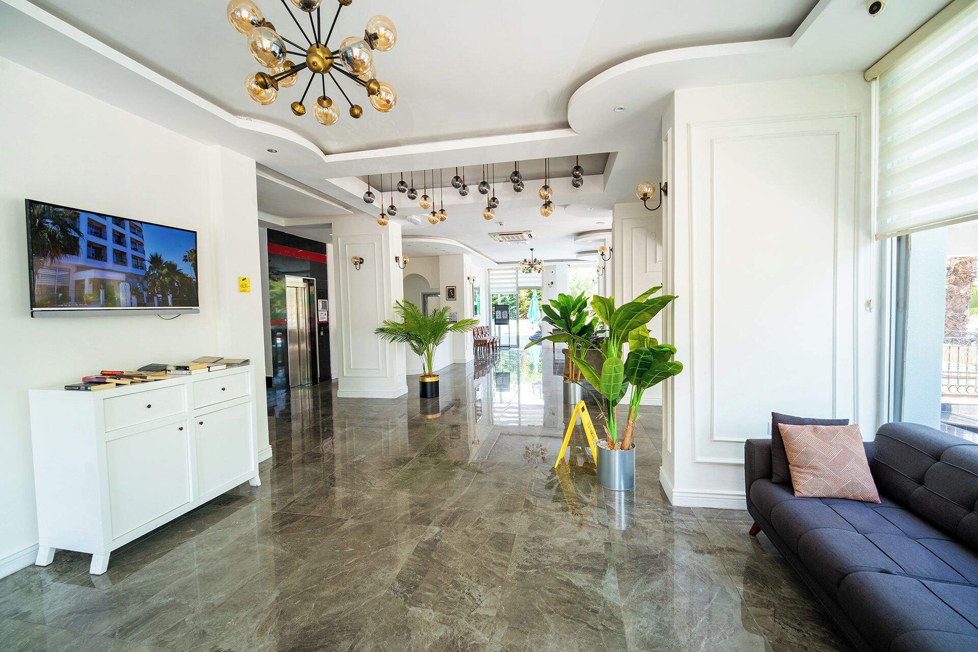 Um hall espaçoso com piso de mármore, um sofá, uma televisão e várias luminárias pendentes.