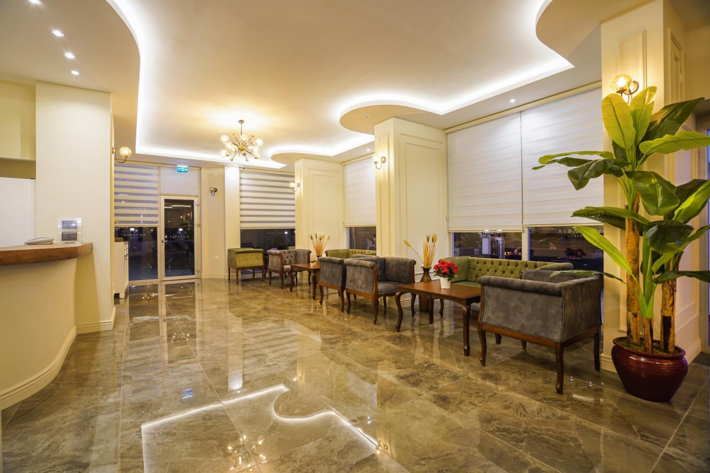 A spacious lobby with a marble floor, seating area with sofas and chairs, a reception desk, and a large potted plant.