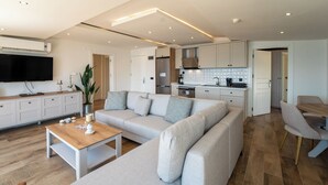 A modern living room with a large L-shaped sofa, a wooden coffee table, and a flat-screen TV mounted on the wall. - Aurasia SeaSide Hotel (Marmaris)