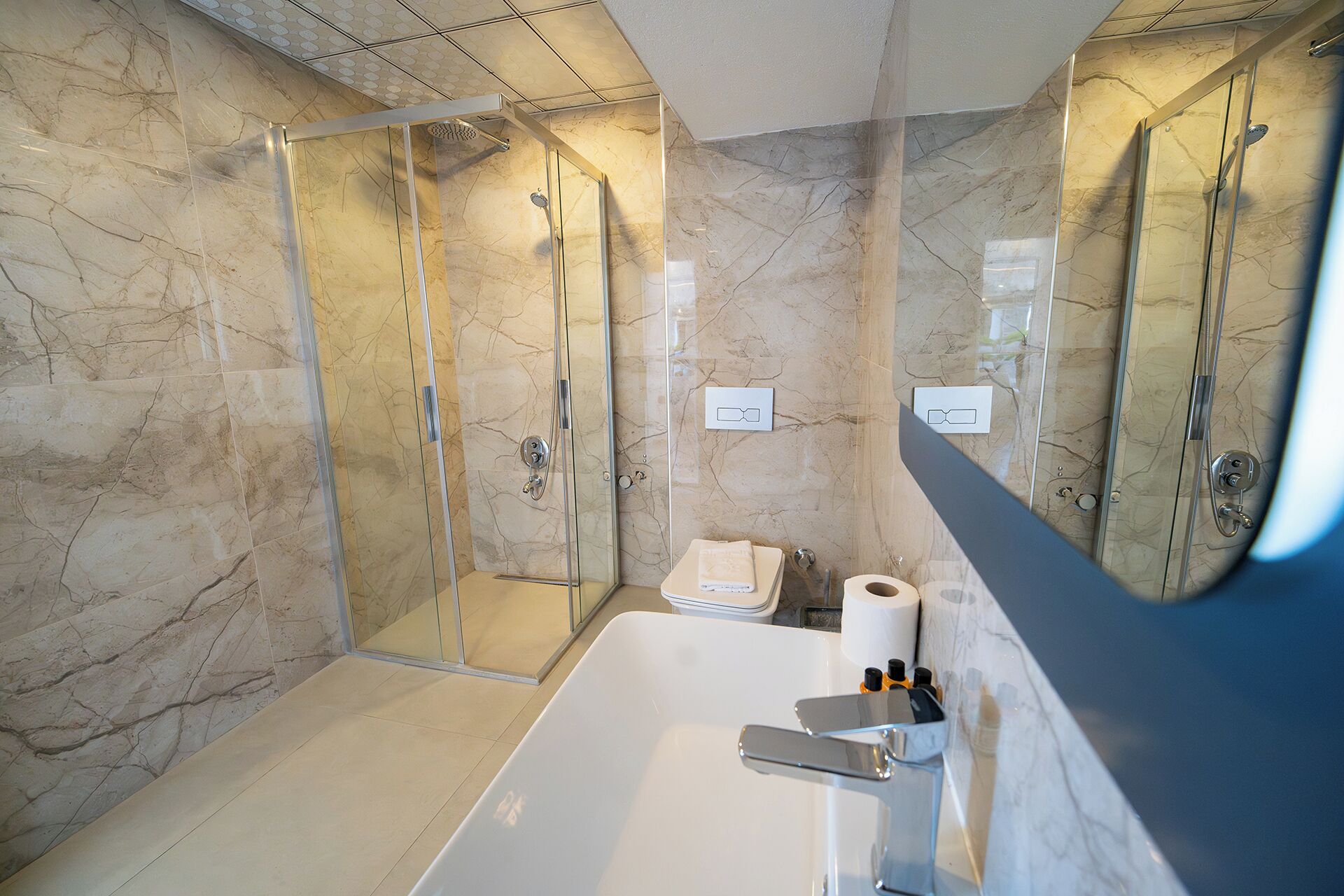 A modern bathroom with a glass-enclosed shower, a white bathtub, and marble walls.