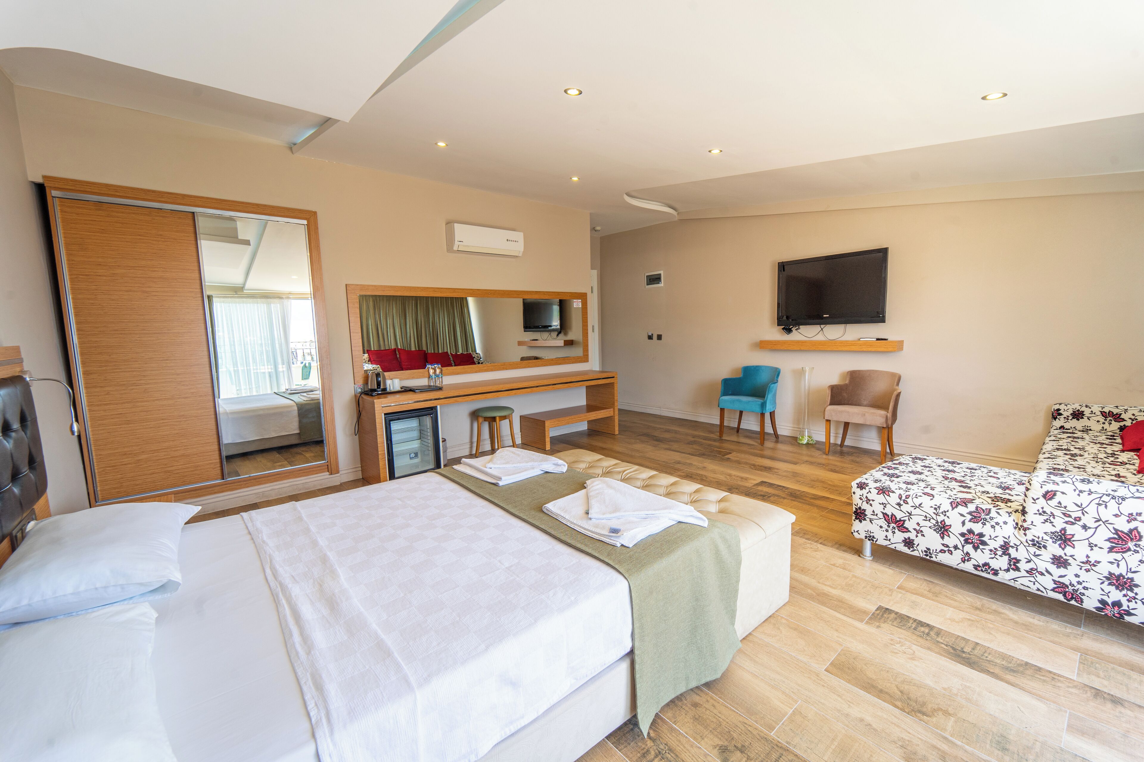 A hotel room with a bed, a desk with a chair, a TV, and a sofa.