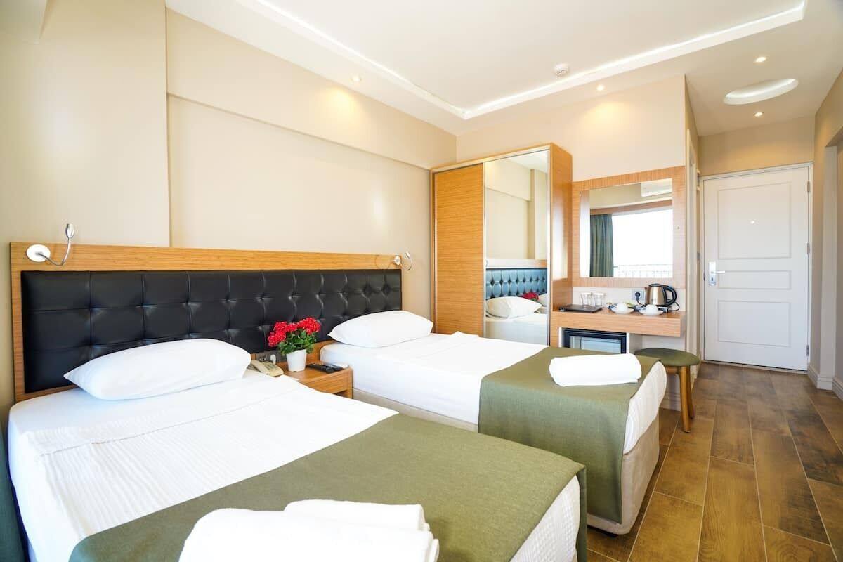 A hotel room with two beds, a small desk, a mirror, and a door.
