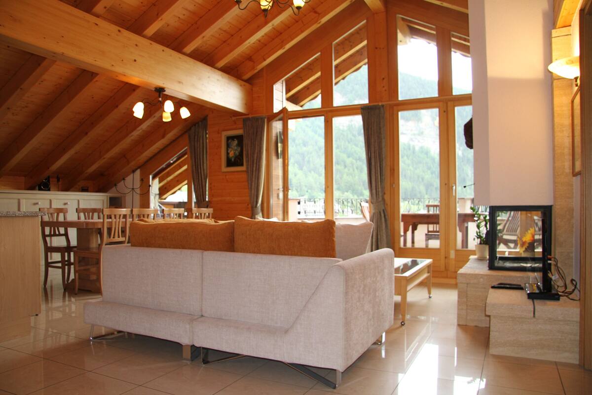 Ein großzügiger Wohnbereich mit einer Couch, Holzboden, großen Fenstern und einem Kamin.