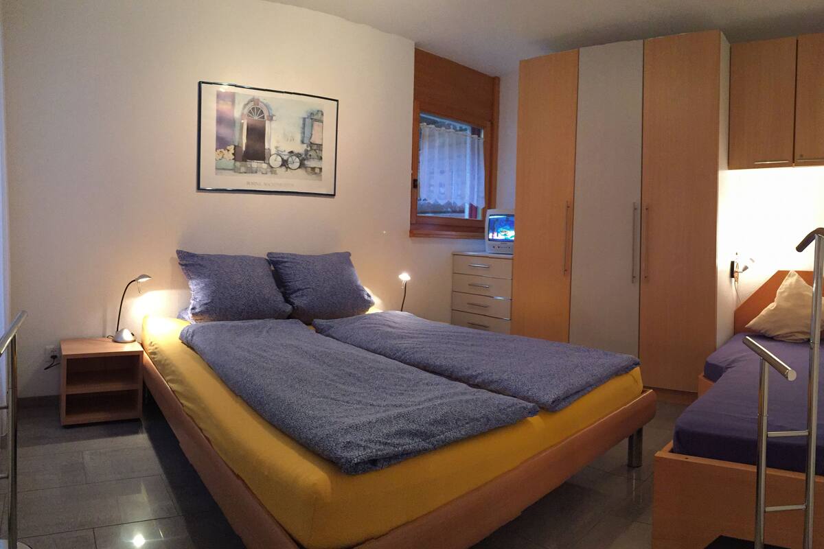 Ein Schlafzimmer mit Bett, Schreibtisch, Stuhl, Kleiderschrank und einem Fenster mit Vorhängen.