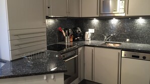 Une cuisine moderne dotée d’un plan de travail en granit noir, d’appareils électroménagers en acier inoxydable et de meubles blancs.