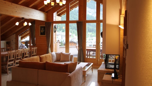 Un intérieur chaleureux avec des éléments en bois, comprenant un canapé, une table à manger et des chaises. De grandes fenêtres offrent une vue sur l’extérieur.