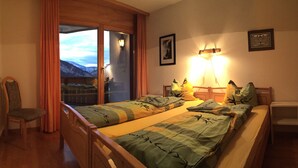 Une chambre avec deux lits, une chaise, une table de chevet et une vue sur les montagnes, visible à travers une porte coulissante.