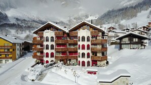Un hôtel à plusieurs étages doté de balcons, avec une piste de ski en arrière-plan et un paysage enneigé.