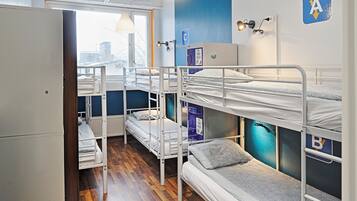 Un dormitorio con literas, un radiador y una ventana con vistas a edificios.