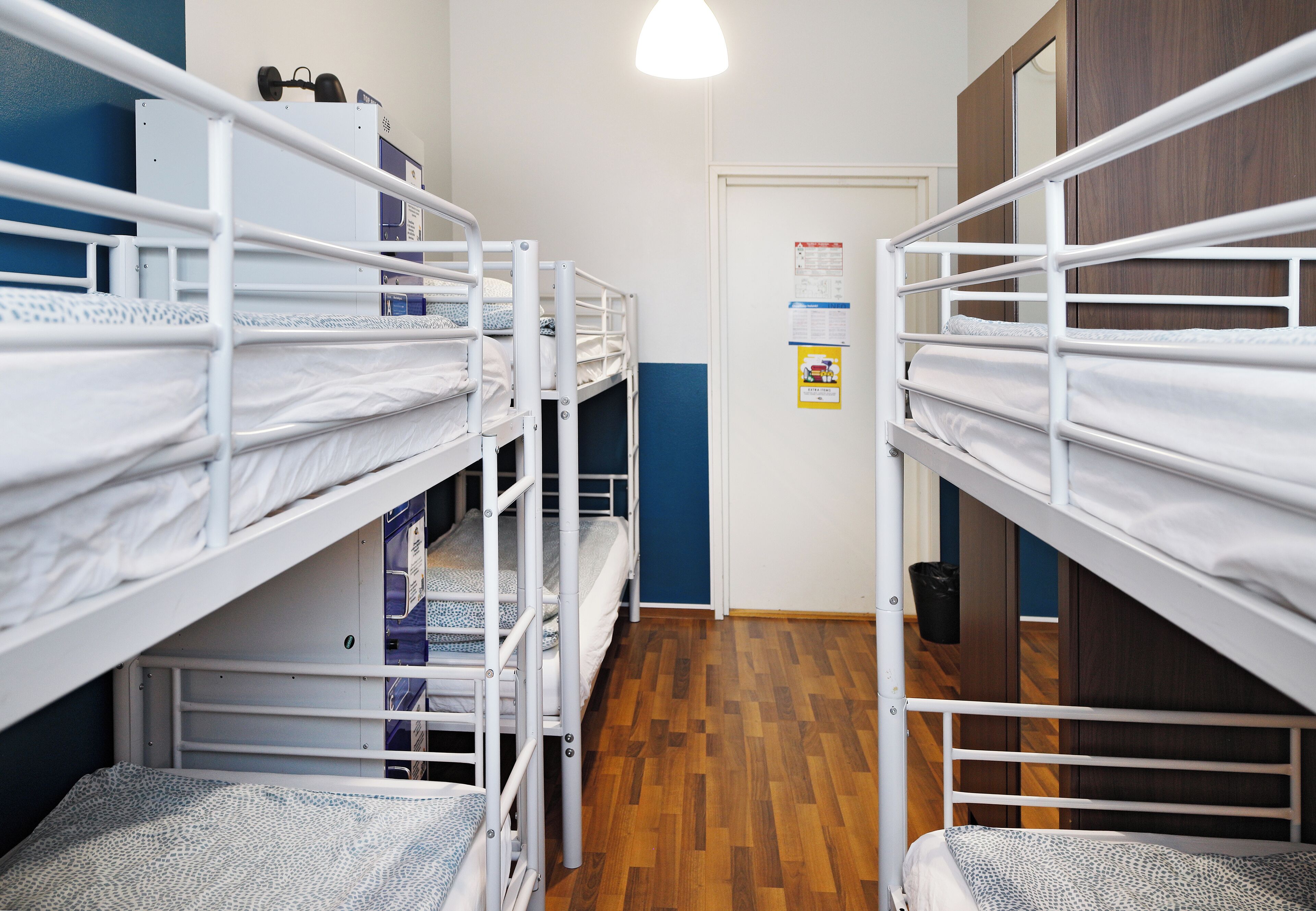 A dormitory room with bunk beds, a wooden floor, and a door with a bulletin board.