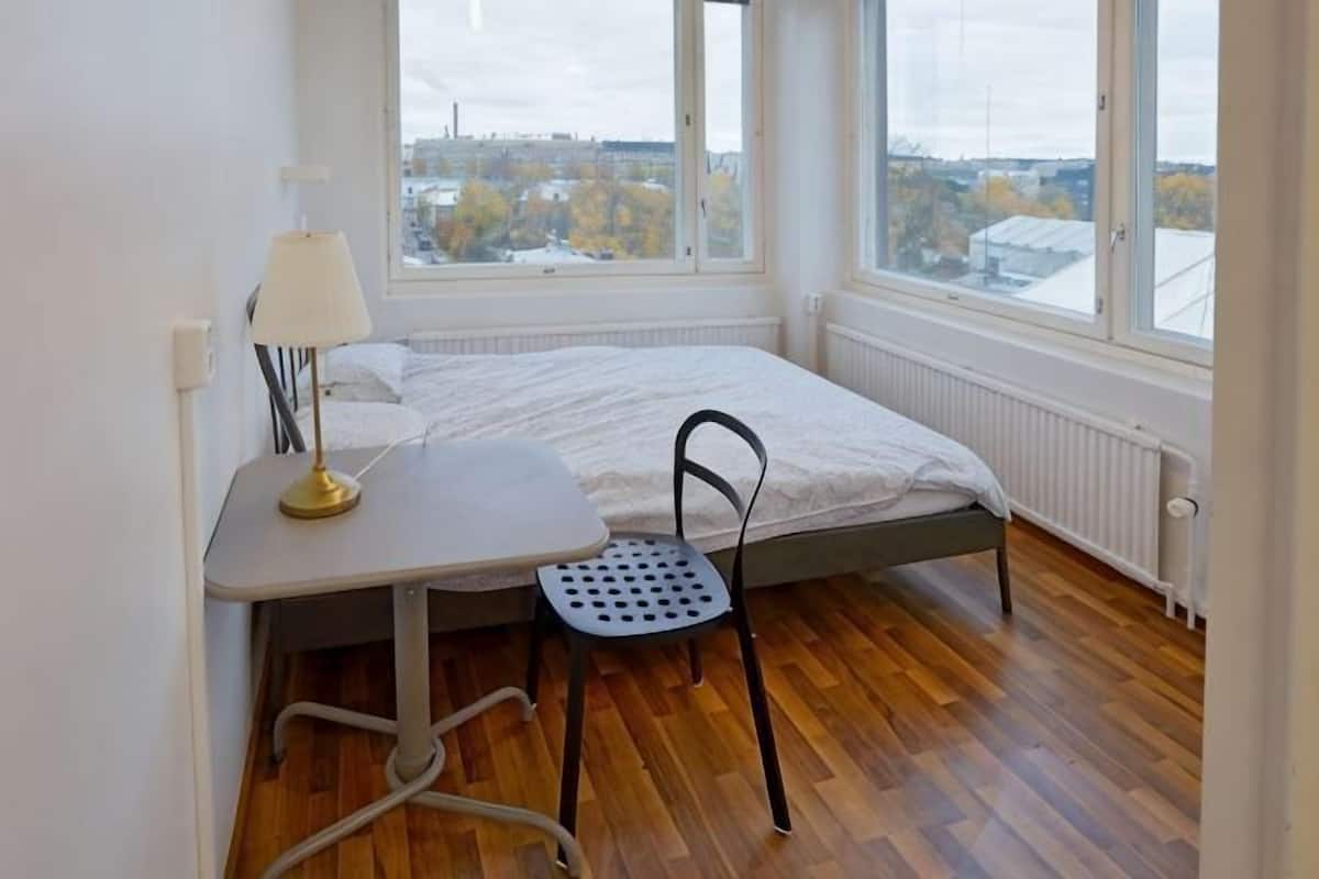 Une chambre Ă coucher avec un lit, un bureau, une chaise et de grandes fenĂŞtres.