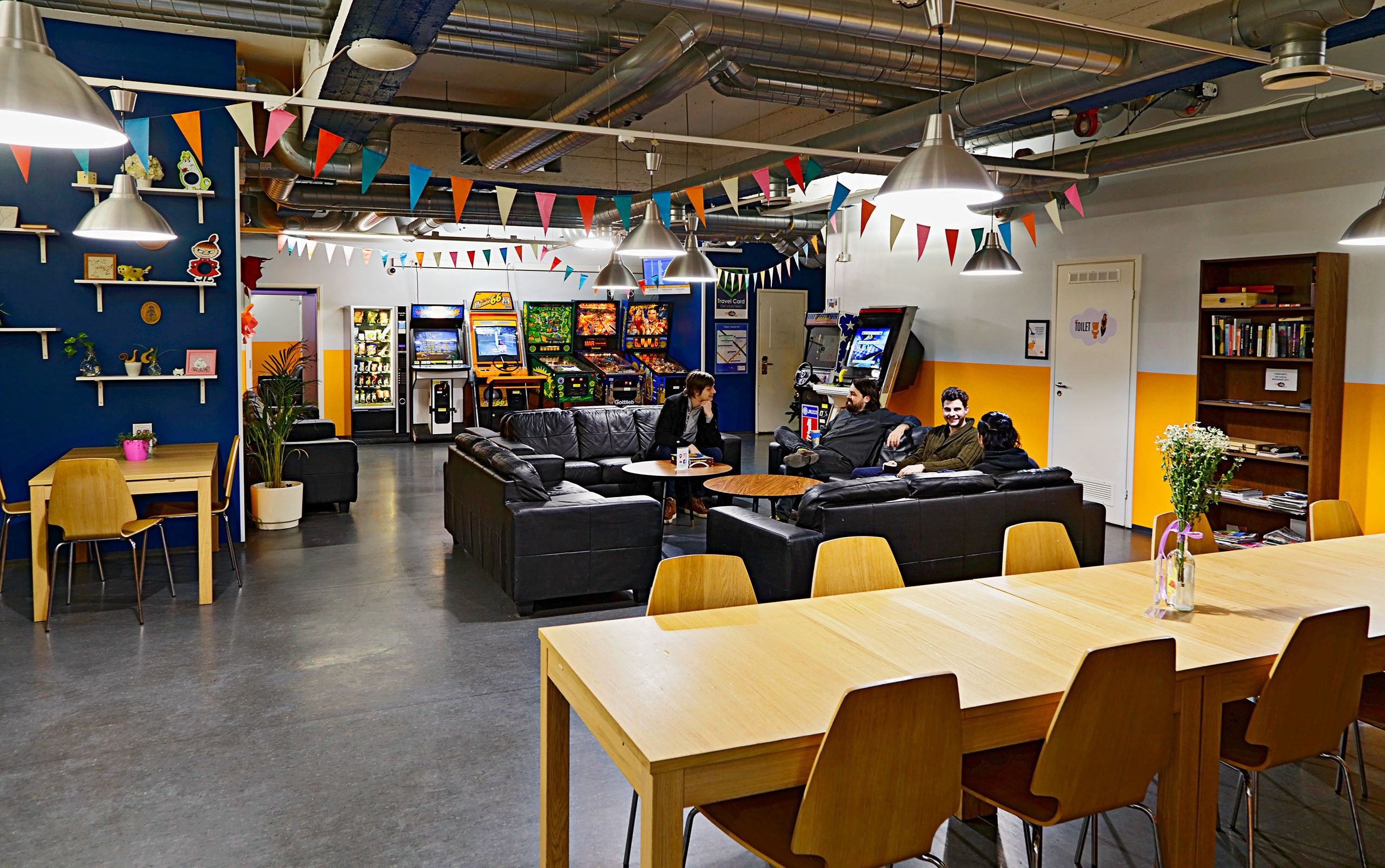 A modern lounge area with leather couches, wooden tables, and gaming machines.