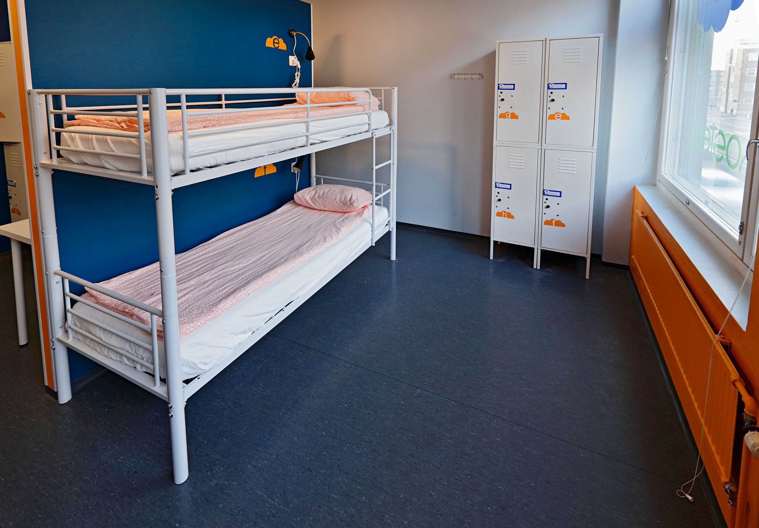 A bunk bed room with a blue wall, a window with a view, and a set of lockers.