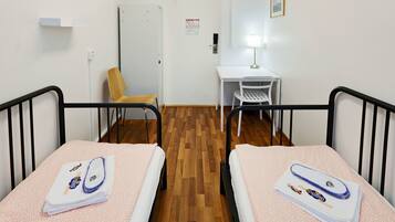 Een hotelkamer met twee eenpersoonsbedden, een bureau, een stoel en een houten vloer.