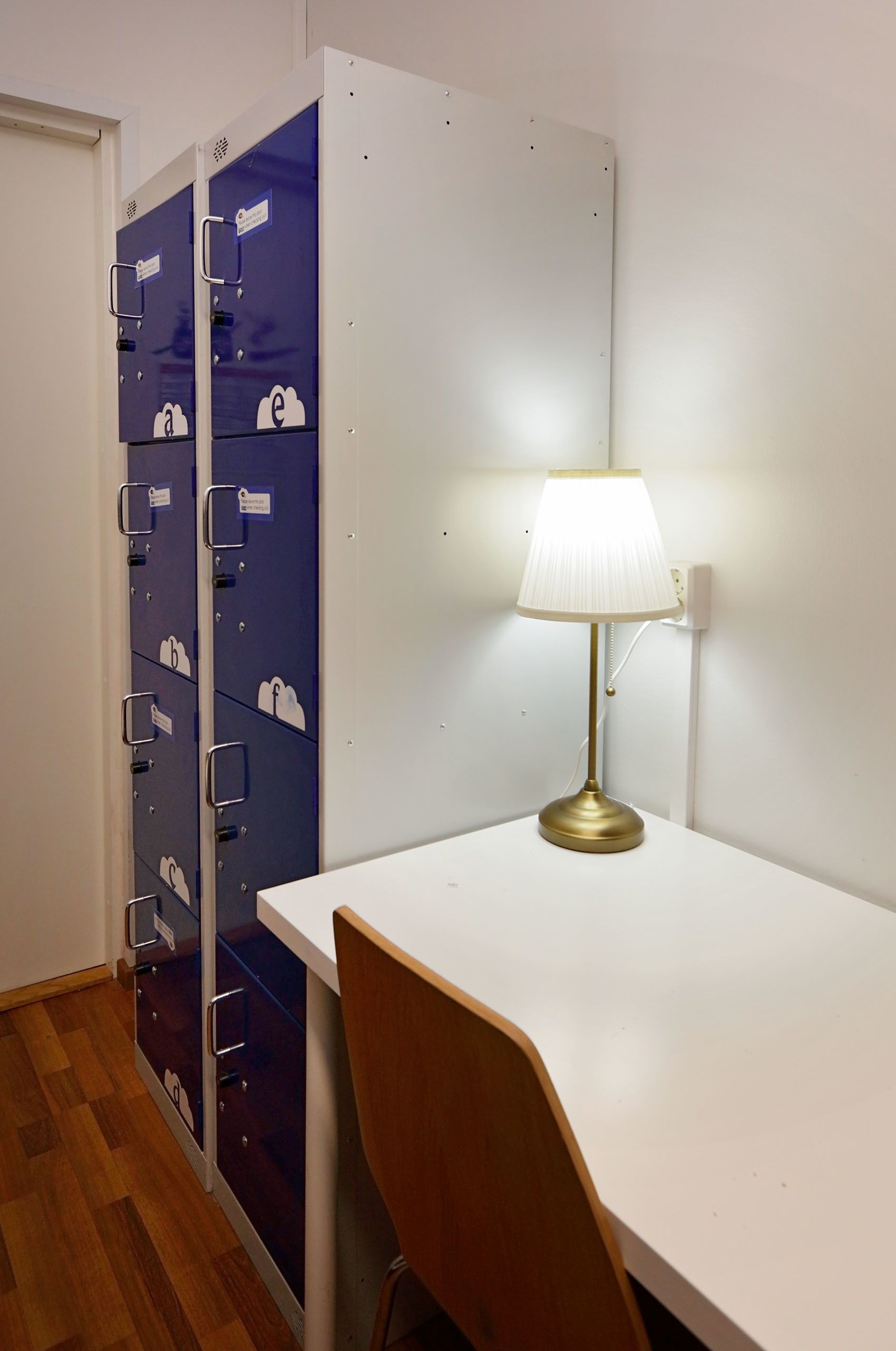 A room with a white desk, a lamp, and a set of blue lockers with white cloud icons.