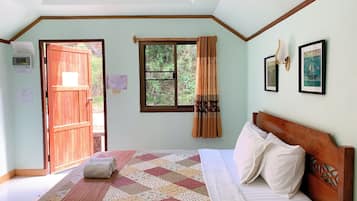 A bedroom with a wooden bed, a quilt, a window with curtains, and a view of greenery outside.
