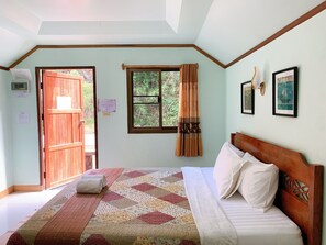Un dormitorio con cama de madera, colcha, ventana con cortinas y vista a follaje exterior.