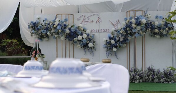 Une réception de mariage avec des décorations florales blanches et bleues, une tente blanche et une table recouverte d’une nappe blanche.