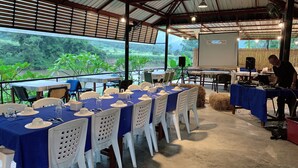 An outdoor dining area with tables set for a meal, overlooking a river and greenery. - Khun Mai Baan Suan Resort (Mae Ai)