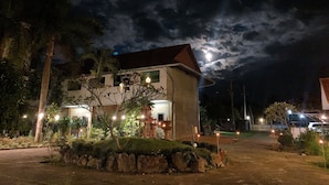 A building with a red roof and white walls, surrounded by greenery and a stone wall. - Khun Mai Baan Suan Resort (Mae Ai)